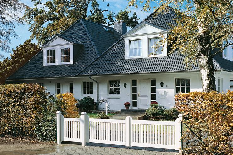 Elegantes zweigeschossiges Haus mit Satteldach, umgeben von Garten und weißem Zaun. Großer Eingangsbereich sichtbar.